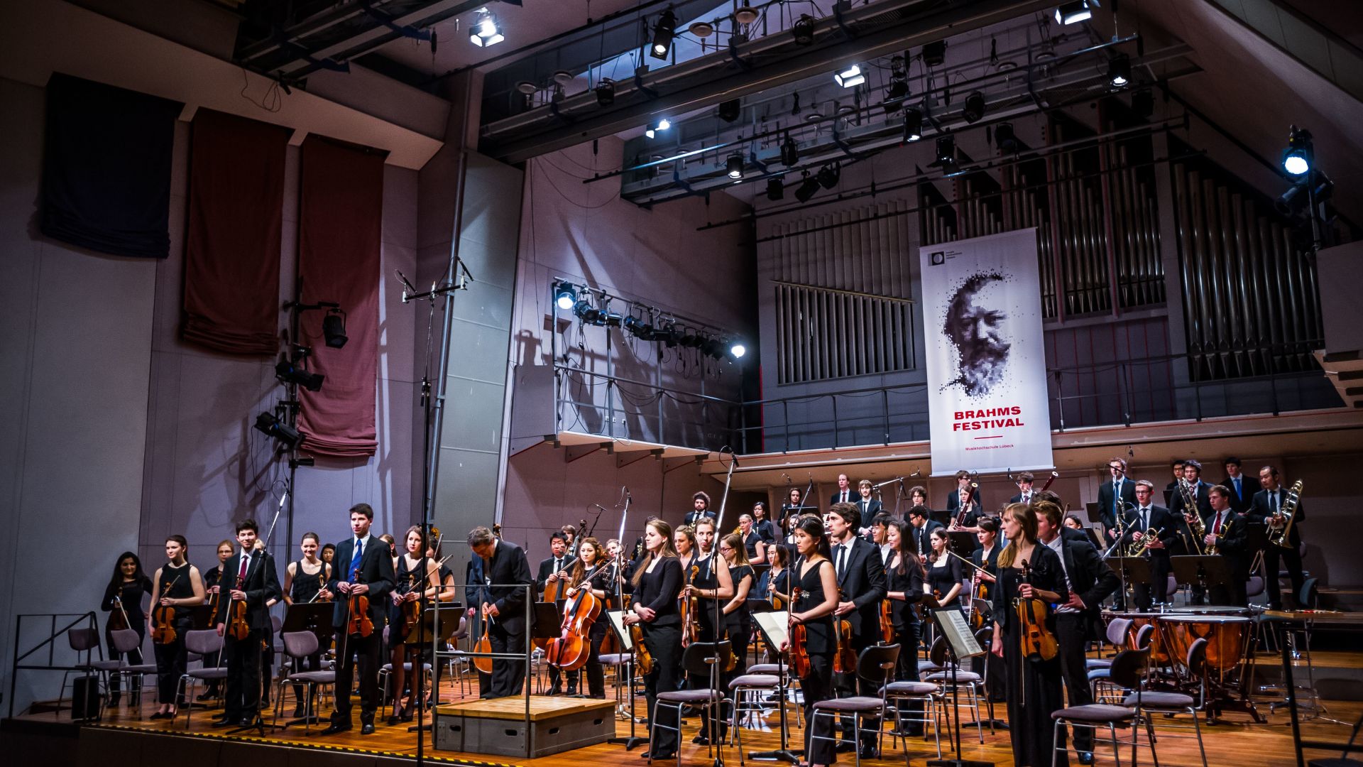 Orchestra on stage during the Brahms Festival in Lübeck, with a large banner in the background.