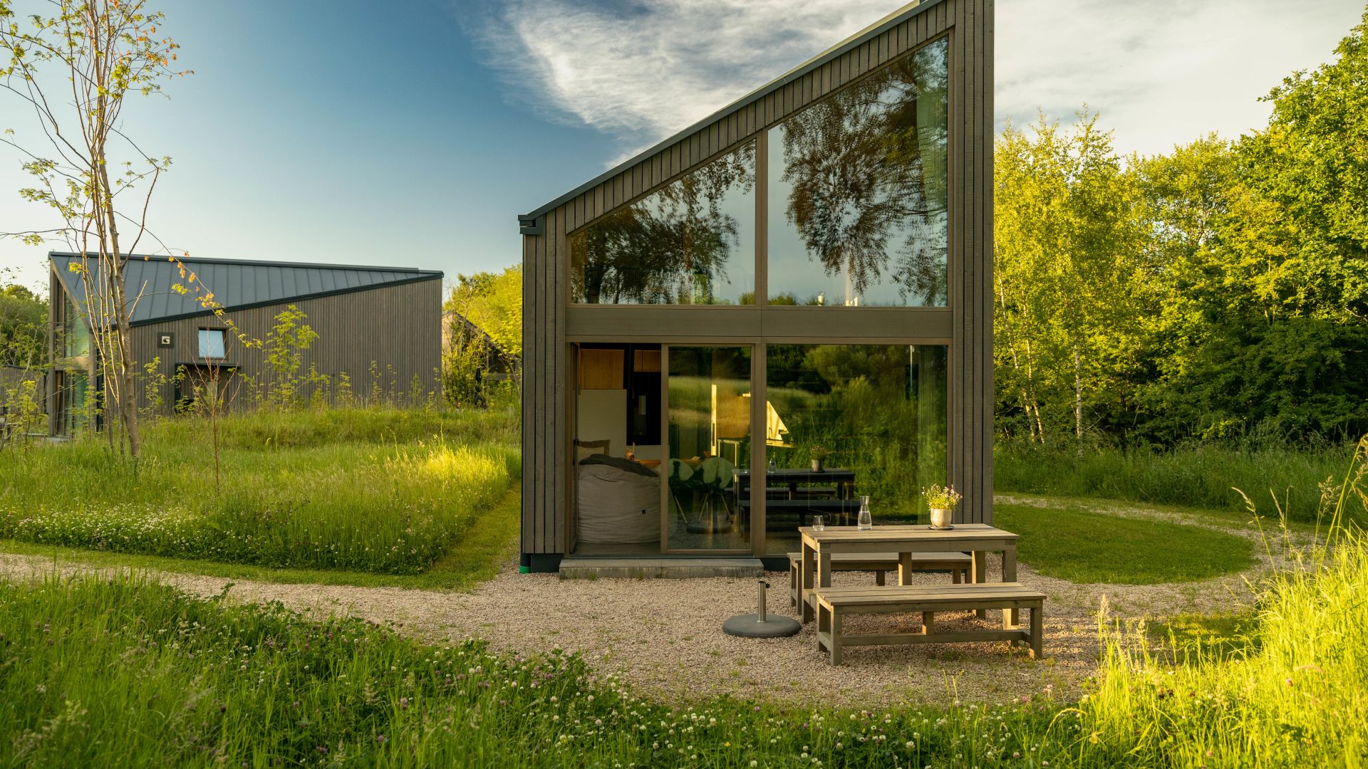 Alojamiento vacacional moderno Neugrad Eifel con grandes ventanas y terraza, rodeado de naturaleza verde.