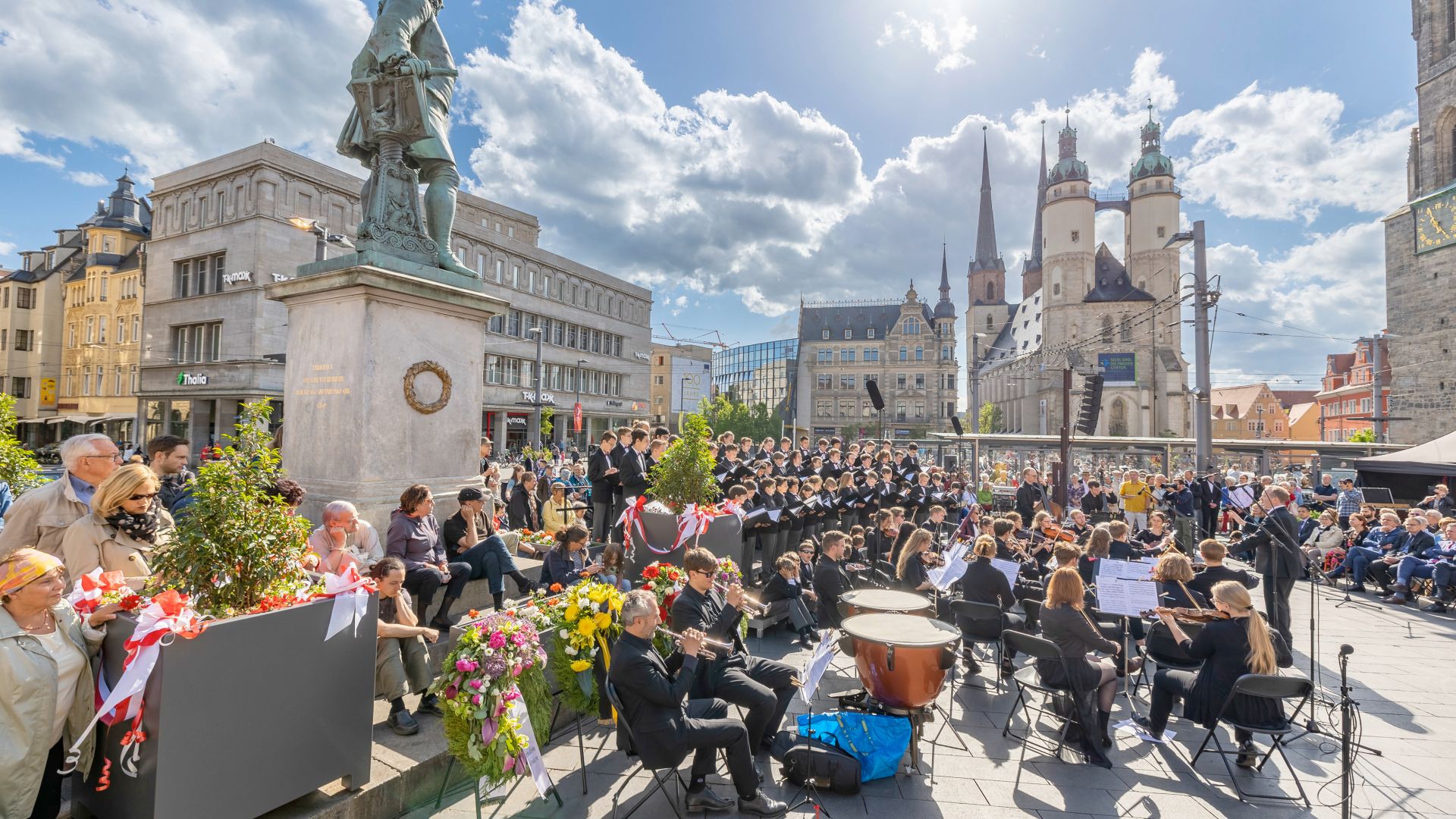 Orchester und Chor führen während der Händel-Festspiele auf dem Marktplatz in Halle (Saale) auf, mit der Marktkirche und dem Händel-Denkmal im Hintergrund.