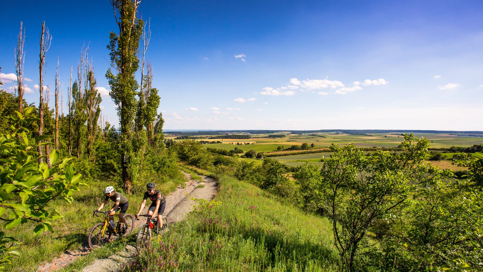 Two cyclists rides through the picturesque landscape of Franconian Tuscany, surrounded by rolling hills.