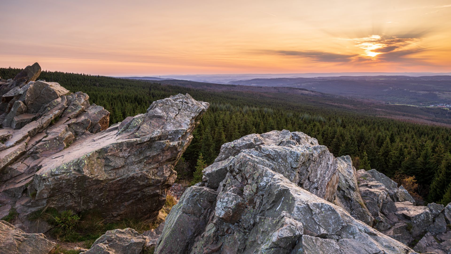 View over the rocks of the Harz Mountains at sunset with forest and distant horizon in the background.