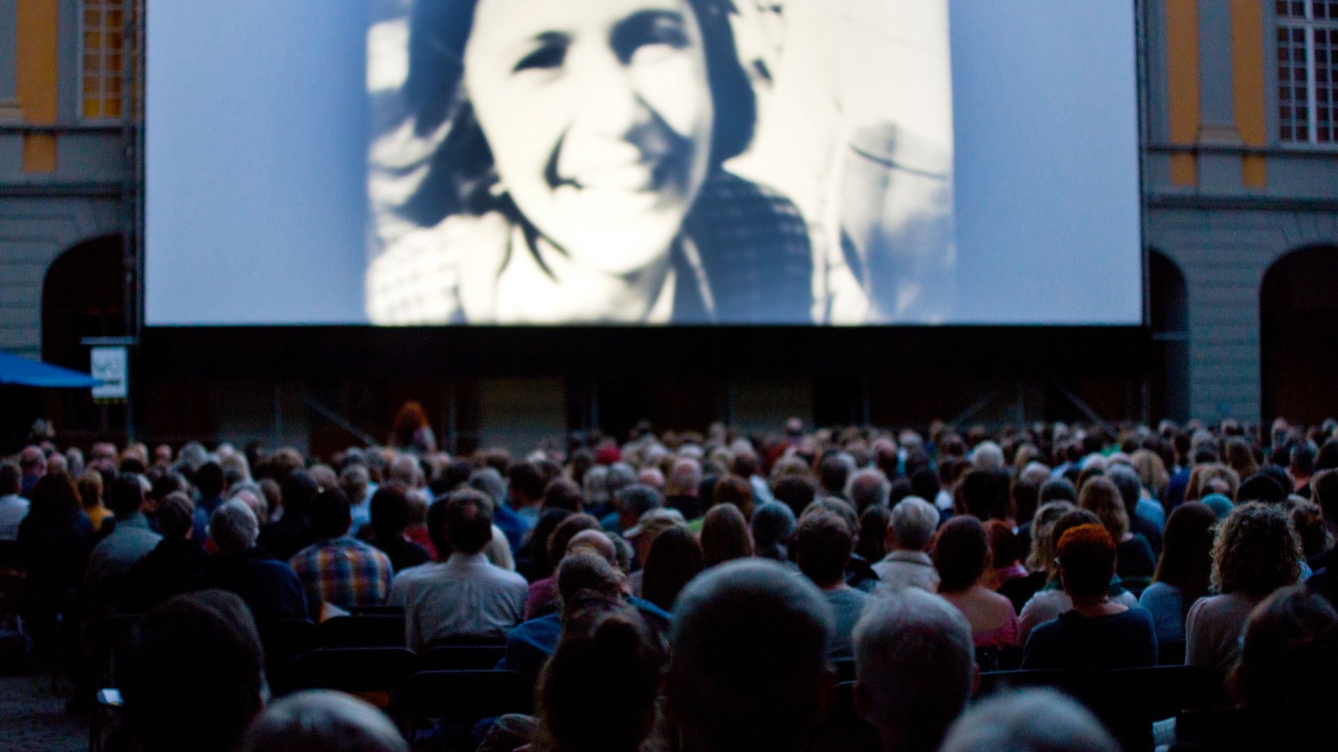 Publikum bei den Internationalen Stummfilmtagen in Bonn, das einen Stummfilm auf einer großen Leinwand im Freien sieht.